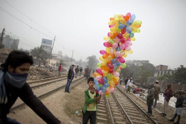 A Bangladeshi boy carries balloons for sale as he watches Muslim devotees walk to attend the final prayer of the three-day Islamic Congregation on the banks of the River Turag in Tongi, 20 kilometers (13 miles) north of the capital Dhaka, Bangladesh, Sunday, January 11, 2015. (Photo by A. M. Ahad/AP Photo)