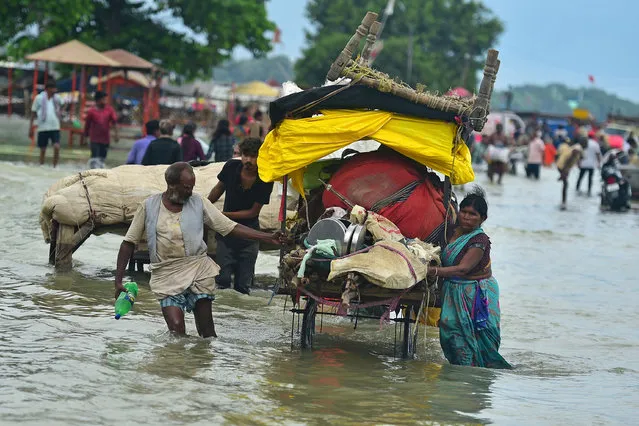 People carrying their belongings wade through flood water on the banks of the Ganges river in Prayagraj on August 6, 2023, after rise in water levels of Ganges and Yamuna river following rainfall. (Photo by Sanjay Kanojia/AFP Photo)