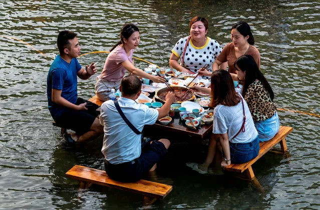People eat hotpot at a table set up in a creek, inside a tourist attraction on a hot day in Chongqing, China on August 21, 2018. (Photo by Reuters/China Stringer Network)