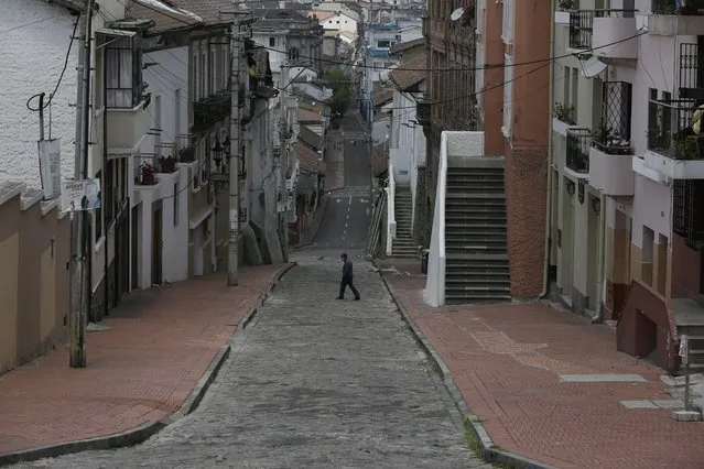 A downtown resident crosses a street free of pedestrians and traffic as a result of new lockdown restrictions due to the increase in COVID-19 infections, in Quito, Ecuador, Saturday, April 24, 2021. (Photo by Dolores Ochoa/AP Photo)