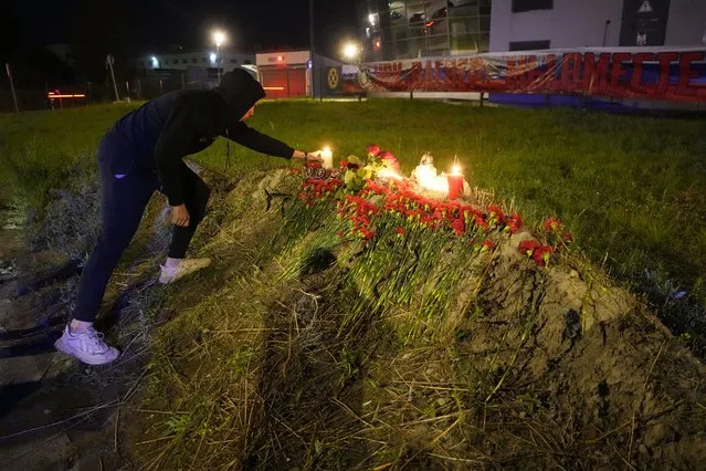 A man lights a candle at an informal memorial next to the former 'PMC Wagner Centre' in St. Petersburg, Russia, Thursday, August 24, 2023, with a banner with words reading 'PMC Wagner, we are together' in the background. Russia's civil aviation agency says mercenary leader Yevgeny Prigozhin was on board a plane that crashed north of Moscow. (Photo by Dmitri Lovetsky/AP Photo)