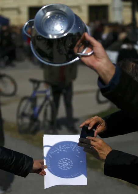 People use a kitchen colander to cast shadows on to white paper during a partial solar eclipse in Vienna March 20, 2015. (Photo by Leonhard Foeger/Reuters)