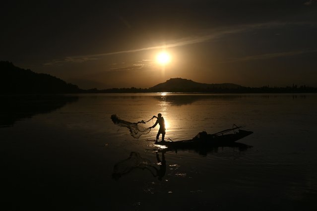 A fisherman casts his net from a boat in Dal Lake as the sun sets in Srinagar on June 24, 2021. (Photo by Tauseef Mustafa/AFP Photo)