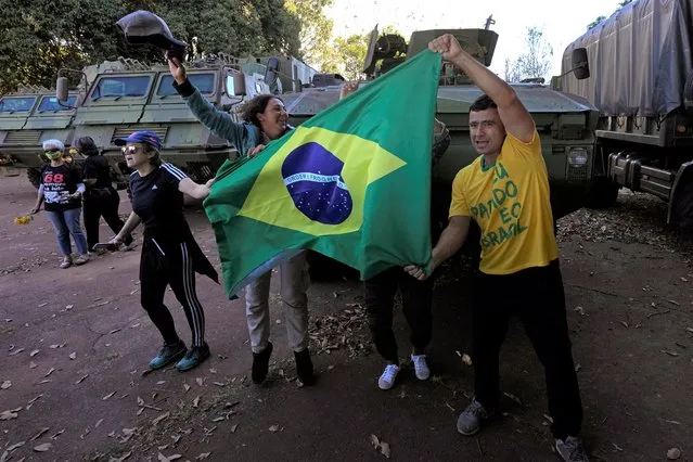Supporters of Brazilian President Jair Bolsonaro cheer with a Brazilian flag as protesters in opposition to the president hold flowers to give to soldiers from a military convoy that paraded by Planalto presidential palace and parked outside the Navy headquarters in Brasilia, Brazil, Tuesday, August 10, 2021. (Photo by Eraldo Peres/AP Photo)