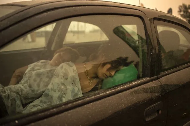 A woman sleeps in her car on the beach as wildfire rages in Pefki village on Evia (Euboea) island, second largest Greek island, on August 8, 2021. Hundreds of Greek firefighters fought desperately on August 8, 2021 to control wildfires on the island of Evia that have charred vast areas of pine forest, destroyed homes and forced tourists and locals to flee. (Photo by Angelos Tzortzinis/AFP Photo)