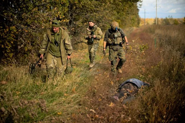 Ukrainian territorial defence deminers walk past a body of a local man who was killed after an explosion of a Russian mine near Grakove village, Ukraine, Thursday, October 13, 2022. (Photo by Francisco Seco/AP Photo)