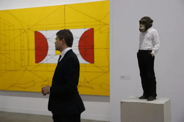 A stands near  artwork “Man with monkey head”, right, created by German artist Stephan Balkenhol during the VIP preview of the art fair “Art Basel” in Hong Kong, Tuesday, March 22, 2016. (Photo by Kin Cheung/AP Photo)