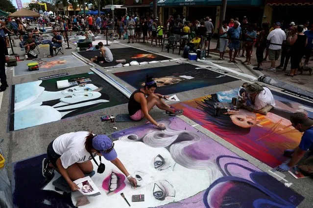 Gina Nolt, of Lake Worth, left and Becca Bartlett, center, of Charleston, SC., work on a chalk painting of the character Effie Trinket from the movie “The Hunger Games”. (Photo by Greg Lovett/The Palm Beach Post)