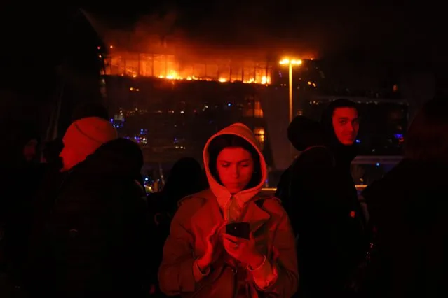 People are seen outside the burning Crocus City Hall concert hall following the shooting incident in Krasnogorsk, outside Moscow, on March 22, 2024. Gunmen opened fire at a concert hall in a Moscow suburb on March 22, 2024 leaving dead and wounded before a major fire spread through the building, Moscow's mayor and Russian news agencies reported. (Photo by AFP Photo/Stringer)