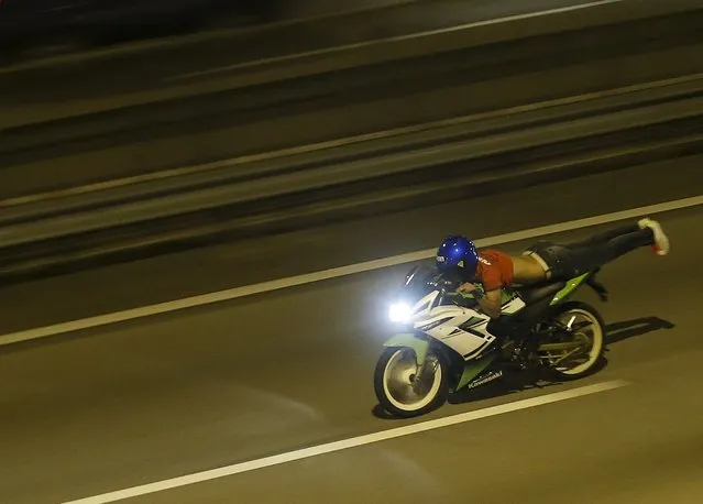 A motorcyclist performs the superman stunt on a highway in Kuala Lumpur, Malaysia, September 14, 2014. Crowds of small motorbikes ridden by racers – or “Mat Rempit”, as they are known in Malaysian slang – face off in impromptu races in the Malaysian capital after dark. The decades-old culture is widely frowned upon by largely conservative Malaysians, who fear its potential to encourage gambling, drug abuse, snatch thefts and sexual promiscuity. (Photo by Olivia Harris/Reuters)