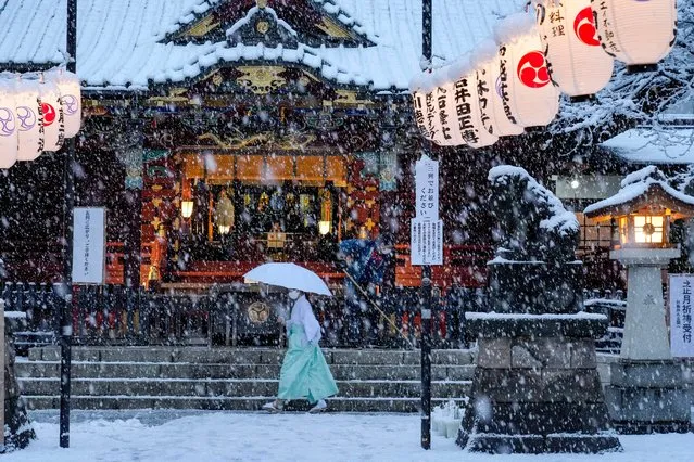 A shrine maiden walks past the main shrine while a worker clears the steps as the snow comes down Thursday, January 6, 2022, in Tokyo. (Photo by Kiichiro Sato/AP Photo)