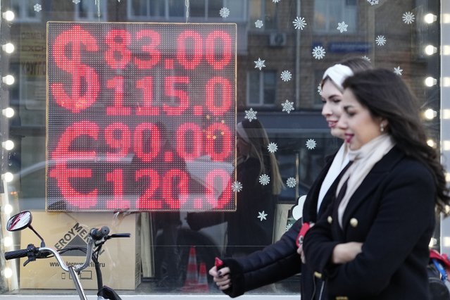 People walk past a currency exchange office screen displaying the exchange rates of U.S. Dollar and Euro to Russian Rubles in Moscow's downtown, Russia, Monday, February 28, 2022. Ordinary Russians are facing the prospect of higher prices as Western sanctions over the invasion of Ukraine sent the ruble plummeting. That's led uneasy people to line up at banks and ATMs on Monday in a country that has seen more than one currency disaster in the post-Soviet era. (Photo by Pavel Golovkin/AP Photo)