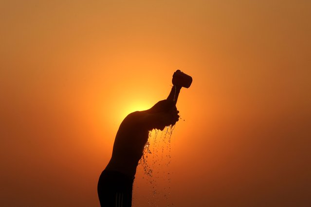 A labourer is silhouetted against the setting sun as he bathes on a hot summer day in Jammu on June 1, 2024. India is no stranger to searing summer temperatures but years of scientific research have found climate change is causing heatwaves to become longer, more frequent and more intense. (Photo by Mukesh Gupta/AFP Photo)