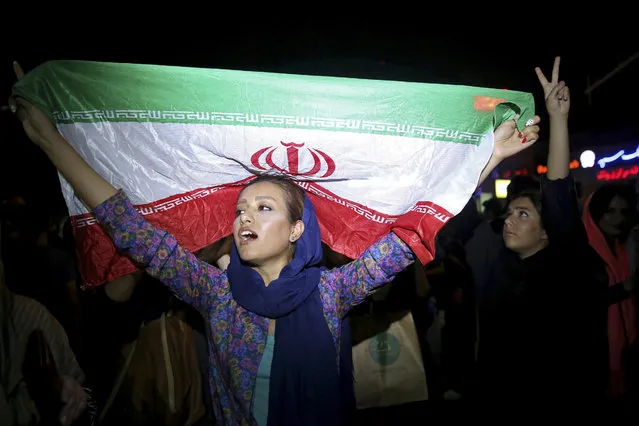 An Iranian woman holds up an Iranian flag as people celebrate a landmark nuclear deal in Tehran, Iran, Tuesday, July 14, 2015. Overcoming decades of hostility, Iran, the United States, and five other world powers struck a historic accord Tuesday to check Tehran's nuclear efforts short of building a bomb. (Photo by Ebrahim Noroozi/AP Photo)