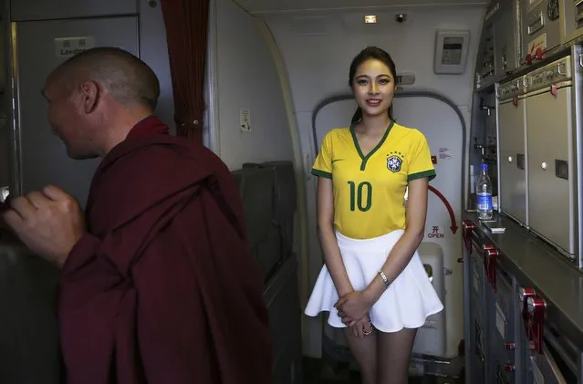 A flight attendant (R) wearing a Brazil soccer team jersey welcomes passengers onto an airplane travelling from Kunming to Hangzhou, in Kunming, Yunnan province June 23, 2014. A Chinese airline company renovated the cabin of one of its flights then dressed the flight attendants with soccer jerseys as a way to celebrate the 2014 Brazil World Cup and hoping to attract more customers, local media reported. (Photo by Wong Campion/Reuters)