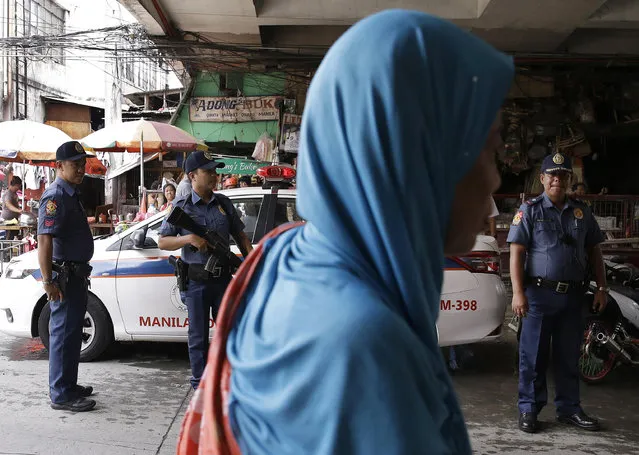 A Muslim woman passes by policemen at a checkpoint in downtown Manila, Philippines, Wednesday, May 24, 2017 as the Philippine National Police is placed under full alert status following the declaration of martial law in Mindanao, southern Philippines. Philippine President Rodrigo Duterte warned Wednesday that he'll be harsh in enforcing martial law in his country's south as he abruptly left Moscow to deal with a crisis at home sparked by a Muslim extremist siege on a city, where militants burned buildings overnight and are feared to have taken hostages. (Photo by Aaron Favila/AP Photo)