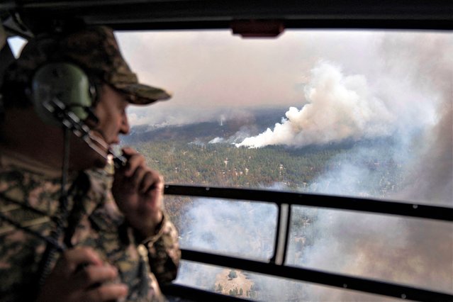 An emergencies ministry specialist looks through a helicopter viewport during an operation to contain wildfires in the eastern Abai region, Kazakhstan on June 12, 2023. (Photo by Turar Kazangapov/Reuters)