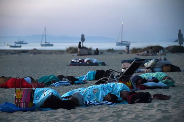 People camp and sleep on the beach in Bormes-les-Mimosas, southern France, at sunrise on July 27, 2017 where they took refuge after being evacuated from their campsite due to the fire. Thousands of tourists fled to the safety of public shelters after a fire broke out overnight in the village of Bormes-les-Mimosas, on the Cote d'Azur, and swept towards the area's campsites. Local residents joined firefighters in southern France on July 26, 2017 to battle blazes that have forced over 10,000 people to flee and left chunks of coastal forest a blackened mess. (Photo by Anne-Christine Poujoulat/AFP Photo)
