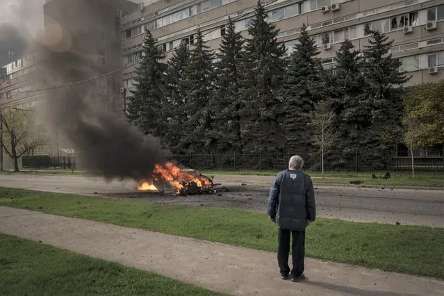 A man watches as a car burns with two people inside, after a Russian bombardment in Kharkiv, Ukraine, Thursday, April 21, 2022. (Photo by Felipe Dana/AP Photo)
