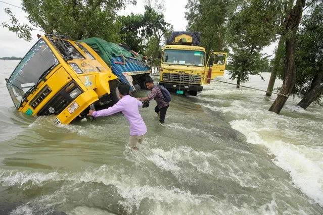 People wade past stranded trucks on a flooded street in Sunamganj on June 21, 2022. Floods are a regular menace to millions of people in low-lying Bangladesh, but experts say climate change is increasing their frequency, ferocity and unpredictability. (Photo by Mamun Hossain/AFP Photo)