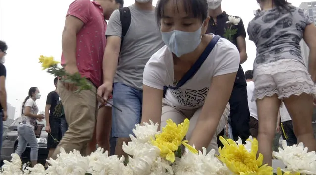 Residents of the Harbour City apartment complex place flowers at a memorial near their building for victims of the Tianjin blasts in northeastern China's Tianjin municipality Tuesday, August 18, 2015. Thunderstorms on Tuesday complicated recovery efforts from last week's massive deadly explosions at a warehouse in China's Tianjin port that exposed dangerous chemicals – including some that could become flammable on contact with water. (Photo by Paul Traynor/AP Photo)