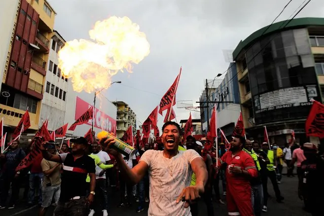 A protester sprays fire during a march against the high cost of food and gasoline in Panama City, on July 12, 2022. Despite the government's announcement on a solution to the population's petitions, thousands of people marched on Tuesday against rising product prices and corruption in Panama. (Photo by Rogelio Figueroa/AFP Photo)