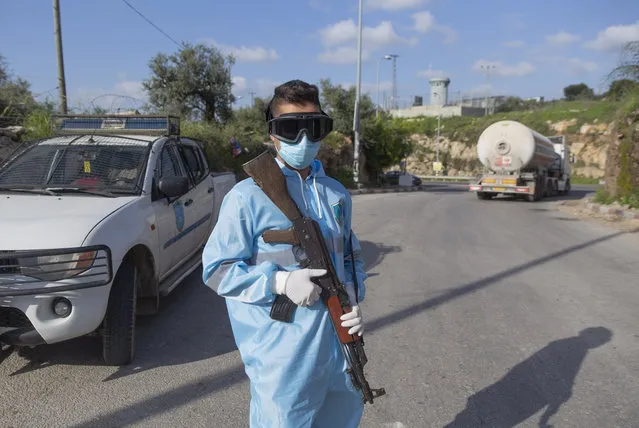 Palestinian policeman mans a checkpoint to receive and register laborers exiting an Israeli army checkpoint, on their way home at the end of a day work in Israel, part of a strict precautionary measures to contain coronavirus outbreak, near the bordering West Bank village of Nilin, west of Ramallah, Wednesday, March 25, 2020. (Photo by Nasser Nasser/AP Photo)