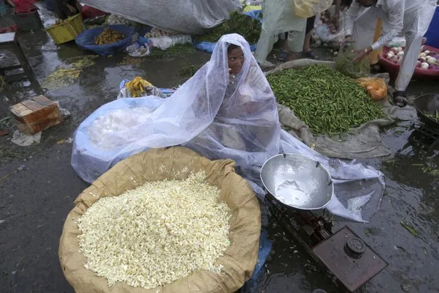 A vendor covers herself with a plastic sheet to protect from rain while she waits for customers at a market, in Lahore, Pakistan, Thursday, July 21, 2022. (Photo by K.M. Chaudary/AP Photo)