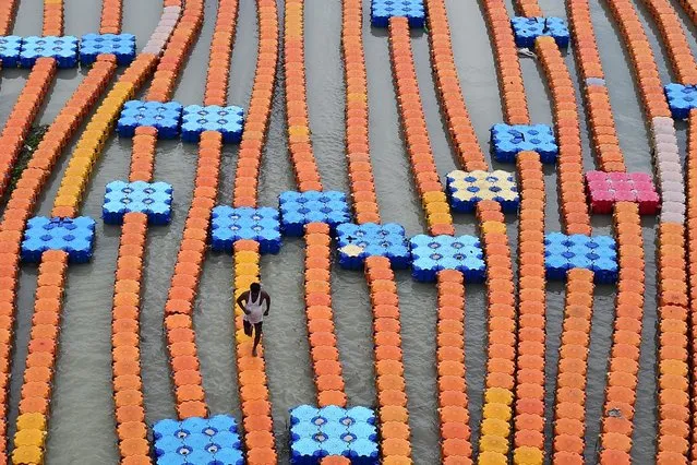 A boatman walks on a floating dock made of plastic cubes along the flooded banks of river Ganges after a rise in the water level due to heavy rains in Allahabad on July 30, 2022. (Photo by Sanjay Kanojia/AFP Photo)