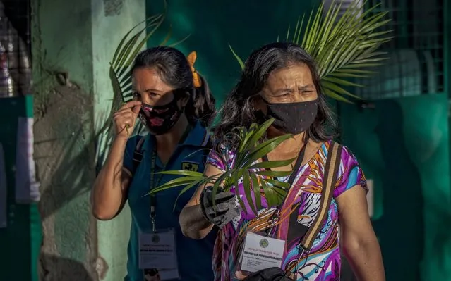 Catholic devotees wearing facemasks hold palm fronds outside their homes as they wait for a priest to bless them with holy water as they celebrate Palm Sunday on April 5, 2020 in Quezon city, Metro Manila, Philippines. Palm Sunday takes place each year on the Sunday before Easter, when the triumphal entry of Jesus into Jerusalem is celebrated in many Christian churches by processions in which palm fronds are carried. Amid the coronavirus pandemic, the Philippine government has banned religious gatherings as part of social distancing measures to prevent the spread of the virus. Catholic devotees have been advised to wait outside their homes for a priest to bless their palm fronds, or to stay inside their homes to hear mass online. The Philippines is the only Roman Catholic majority in Southeast Asia with around 85% practicing the faith. (Photo by Ezra Acayan/Getty Images)