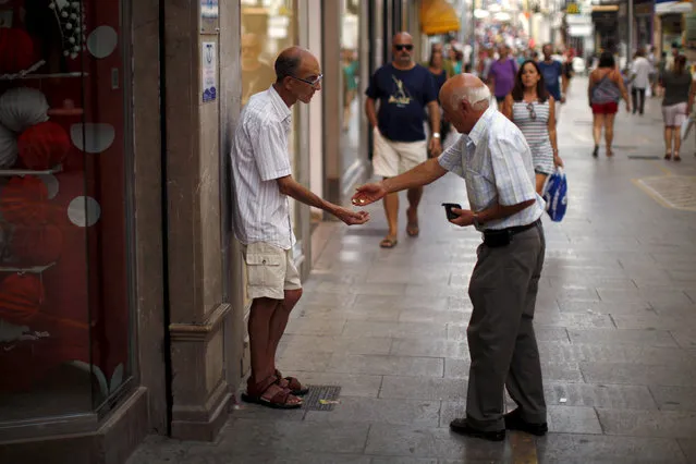 A man gives coins to a beggar at La Bola street in downtown Ronda, southern Spain, August 27, 2015. (Photo by Jon Nazca/Reuters)