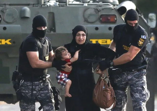 Two Hungarian riot policemen escort a migrant woman and her child in Roszke, Hungary September 16, 2015. Serbia on Wednesday condemned Hungary's use of water cannon and tear gas against migrants on their border, saying Hungary had “no right” to do so, the Serbian state news agency Tanjug reported. (Photo by Dado Ruvic/Reuters)