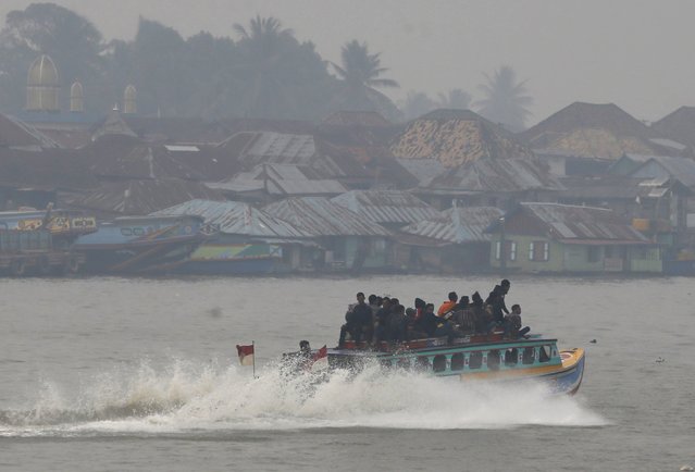 Passengers sit on the top deck of a wooden boat as it traverses a haze shrouded Musi River in Palembang, on the Indonesian island of Sumatra, September 20, 2015. (Photo by Reuters/Beawiharta)
