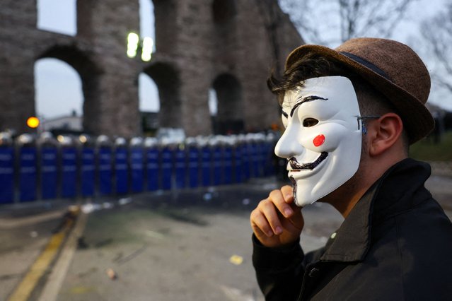 A person wears a Guy Fawkes mask as police officers stand guard during a protest on the day Istanbul Mayor Ekrem Imamoglu was jailed as part of a corruption investigation, in Istanbul, Turkey, on March 23, 2025. (Photo by Murad Sezer/Reuters)