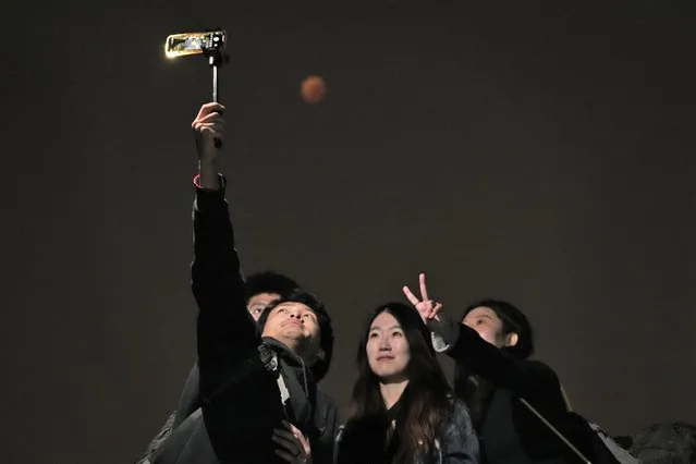 Residents pose for a selfie as the moon rises during a lunar eclipse in Beijing, China, Tuesday, November 8, 2022. (Photo by Ng Han Guan/AP Photo)