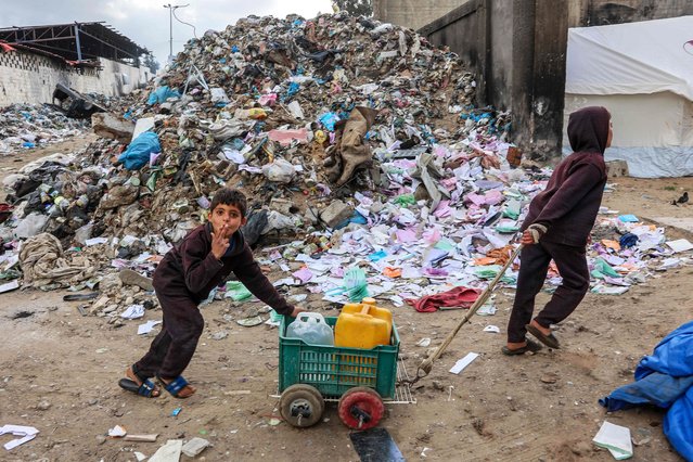 A displaced Palestinian child gestures as he pushes a cart carrying water containers near a camp set up at a landfil in the Yarmuk area in Gaza City on March 20, 2025. Israel bombarded Gaza and pressed its ground operations on March 20, after issuing what it called a “last warning” for Palestinians to return hostages and remove Hamas from power. (Photo by Omar Al-Qattaa/AFP Photo)