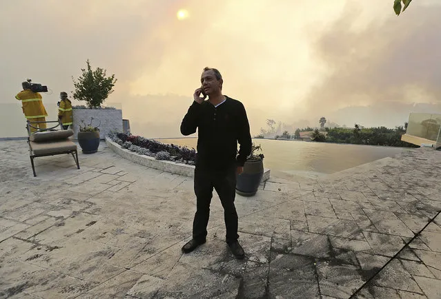 Maurice Kaboud makes a phone call after a wildfire threatened his home in the Bel Air district of Los Angeles Wednesday, December 6, 2017. When firefighters told Kaboud to evacuate, he decided to stay and protect his home. The 59-year-old stood in the backyard of his multimillion- dollar home as the Skirball fire raged nearby. “God willing, this will slow down so the firefighters can do their job”, Kaboud said. (Photo by Reed Saxon/AP Photo)