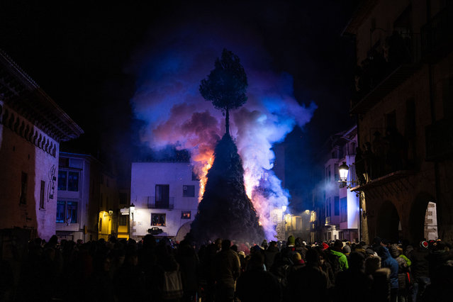 General view of the burning hut as neighbours crowded under the pine tree to cross it inside on January 19, 2024 in Forcall, Spain. The small village of Forcall, with 450 inhabitants, holds an annual festival to celebrate the patron saint of animals, Sant Antoni. Following a procession through the streets of the village with people dressed as demons, and another procession with animals, villagers cross through a big bonfire in the middle of the village square. (Photo by Zowy Voeten/Getty Images)