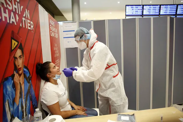 A health worker collects a nasal swab sample for COVID-19 test, at the Roissy Charles de Gaulle airport, outside Paris, Saturday, August 1, 2020. Travelers entering France from 16 countries where the coronavirus is circulating widely are having to undergo virus tests upon arrival at French airports and ports. (Photo by Thibault Camus/AP Photo)