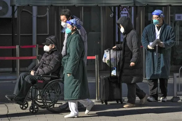 Medical workers in protective gear escort an elderly patient on a wheelchair followed by family members as they leave a fever clinic at a hospital in Beijing on Monday, December 19, 2022. A Chinese health official said that the country would only count those who died from pneumonia or respiratory failure in the official COVID death toll, a narrow definition that would certainly limit the numbers of deaths reported, as the country's reopening progresses and cases have soared. (Photo by Andy Wong/AP Photo)
