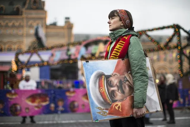An artist holds a portrait of former Soviet leader Josef Stalin outside the GUM, State Department store decorated with New Year and Christmas illumination in Moscow's Red Square, Thursday, December 21, 2017. Communist supporters marked the anniversary of Stalin's birth on Thursday. (Photo by Alexander Zemlianichenko/AP Photo)