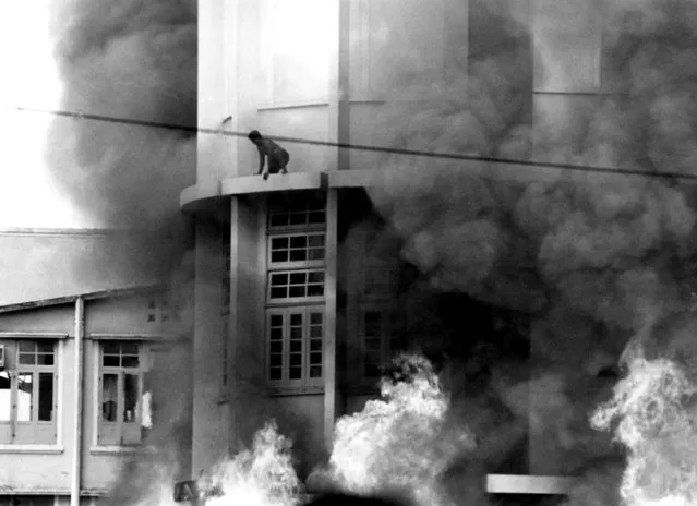 The janitor of a Bangkok building torched by angry students considers leaping to the blazing pavement, Thailand, October 15, 1973. The man drew back, collapsed and burned to death as the structure went up in flames.  Protests over military government ended in riots, machine gunning of students and the fall of the junta regime. (Photo by AP Photo)