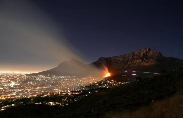 Flames illuminate smoke over the city as strong winds fan a fire that broke out on the slopes of Table Mountain in Cape Town, South Africa, October 31, 2020. Picture taken with long time exposure. (Photo by Mike Hutchings/Reuters)