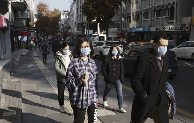 People wearing masks to help protect against the spread of coronavirus, walk, in Ankara, Turkey, Monday, November 15, 2020. Turkish health ministry statistics show 93 people died Friday of COVID-19 amid a surge in infections, bringing the daily death toll to numbers last seen in April. (Photo by Burhan Ozbilici/AP Photo)