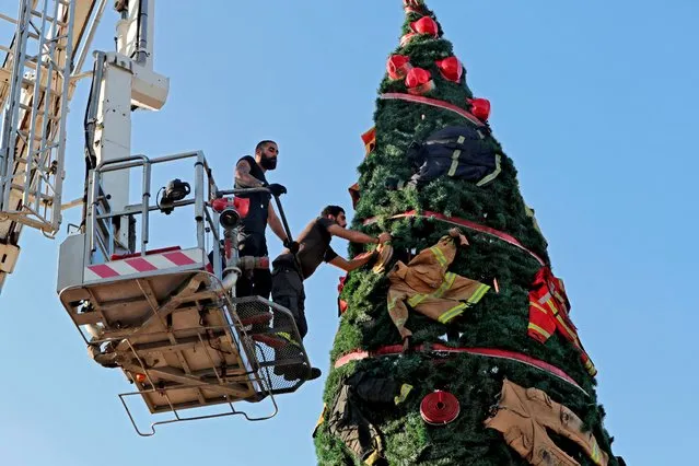 Members of the Lebanese Civil Defense erect a Christmas tree by Lebanese artist Hayat Nazer decorated with uniforms of firefighters as a way to pay tribute to colleagues who were killed in the August 4 port explosion, in the Lebanese capital's harbour on December 18, 2020. (Photo by Anwar Amro/AFP Photo)