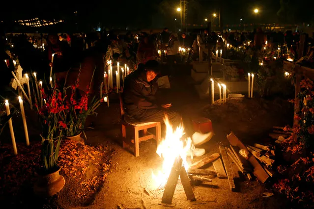 A man stand next to graves on the Day of the Dead by paying homage to his dead relatives at the cemetery of Metepec on the outskirts of Mexico City, Mexico November 1, 2016. (Photo by Carlos Jasso/Reuters)