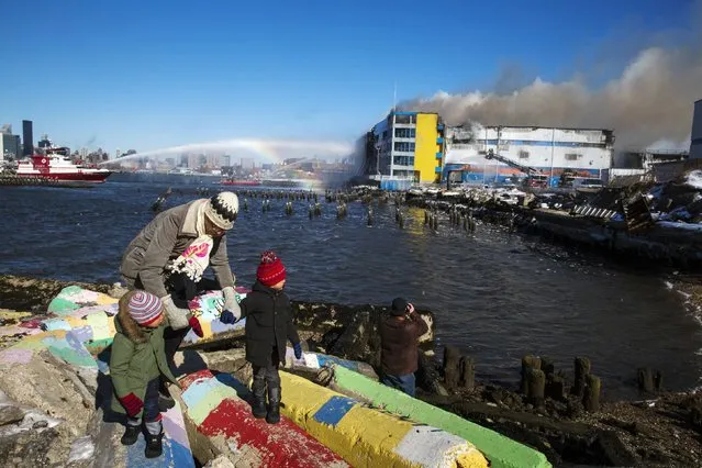 A father leads his two children away after watching members of the New York Fire Department battle a six alarm fire in a storage facility on the waterfront of the East River in New York January 31, 2015. (Photo by Lucas Jackson/Reuters)