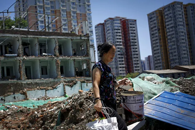 A woman carrying her belonging walks by recently demolished homes near a high-rise residential building in Beijing, Thursday, July 26, 2018. The Chinese capital has undergone rapid redevelopment over the past decades that has seen former residents pushed outside of the city center in favor of commercial development catering to tourism and retail. (Photo by Andy Wong/AP Photo)