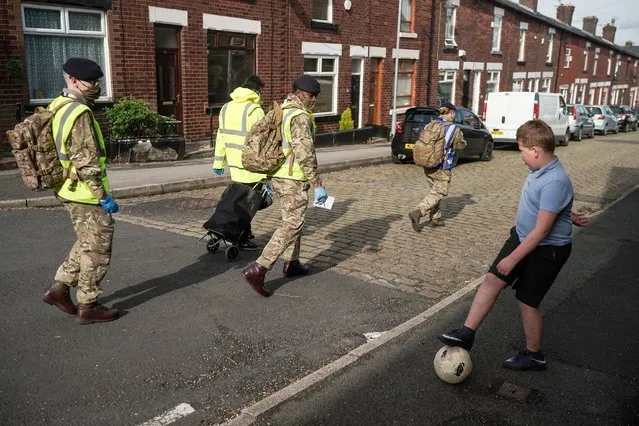 A boy plays football in the street as gunners from the Royal Horse Artillery distribute Covid-19 polymerase chain reaction (PCR) tests to local residents on May 24, 2021 in Bolton, England. The Covid-19 B.1.617.2 virus variant first identified in India has caused a spike in cases in the city. The Army has been brought in to help with surge testing. (Photo by Christopher Furlong/Getty Images)