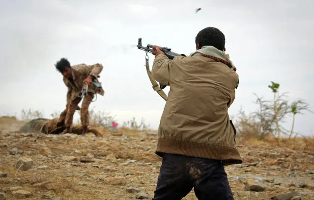 A Yemeni tribesman from the Popular Resistance Committee, supporting forces loyal to Yemen's Saudi-backed President Abedrabbo Mansour Hadi, fires a weapon as a fellow tribesman rescues the body of a dead comrade in the country's third-city of Taez during clashes with Shiite Huthi rebels, on December 19, 2016. (Photo by Ahmad Al-Basha/AFP Photo)